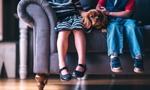 Legs of girl and boy sitting on a sofa with a spaniel sitting between them