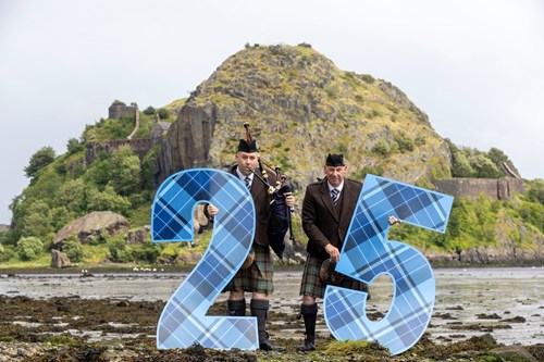 Piper Craig Bell and Drummer Ian MacMillian stand in front of Dumbarton Rock holding a large 2 and 5